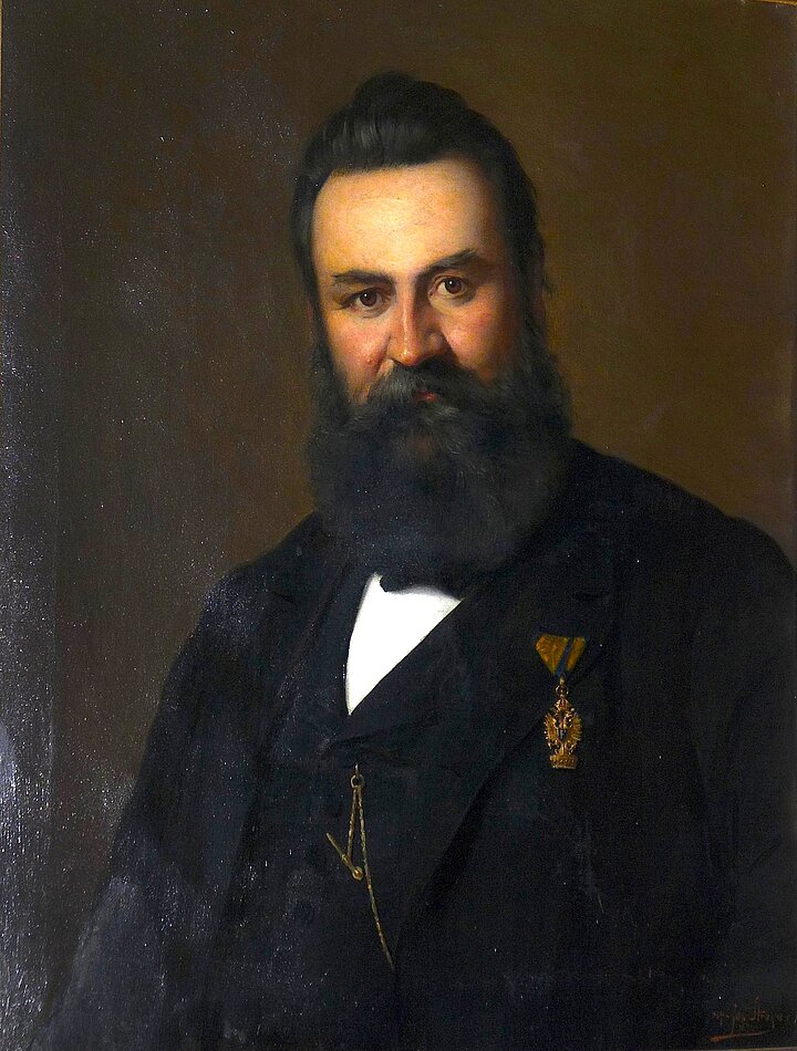 Ein Portrait-Gemälde, das einen Herren mit langem, dunklen Bart im Anzug zeigt.